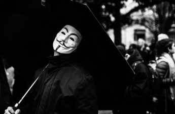 A person wears a mask associated with anonymous, who popularized the term doxxing